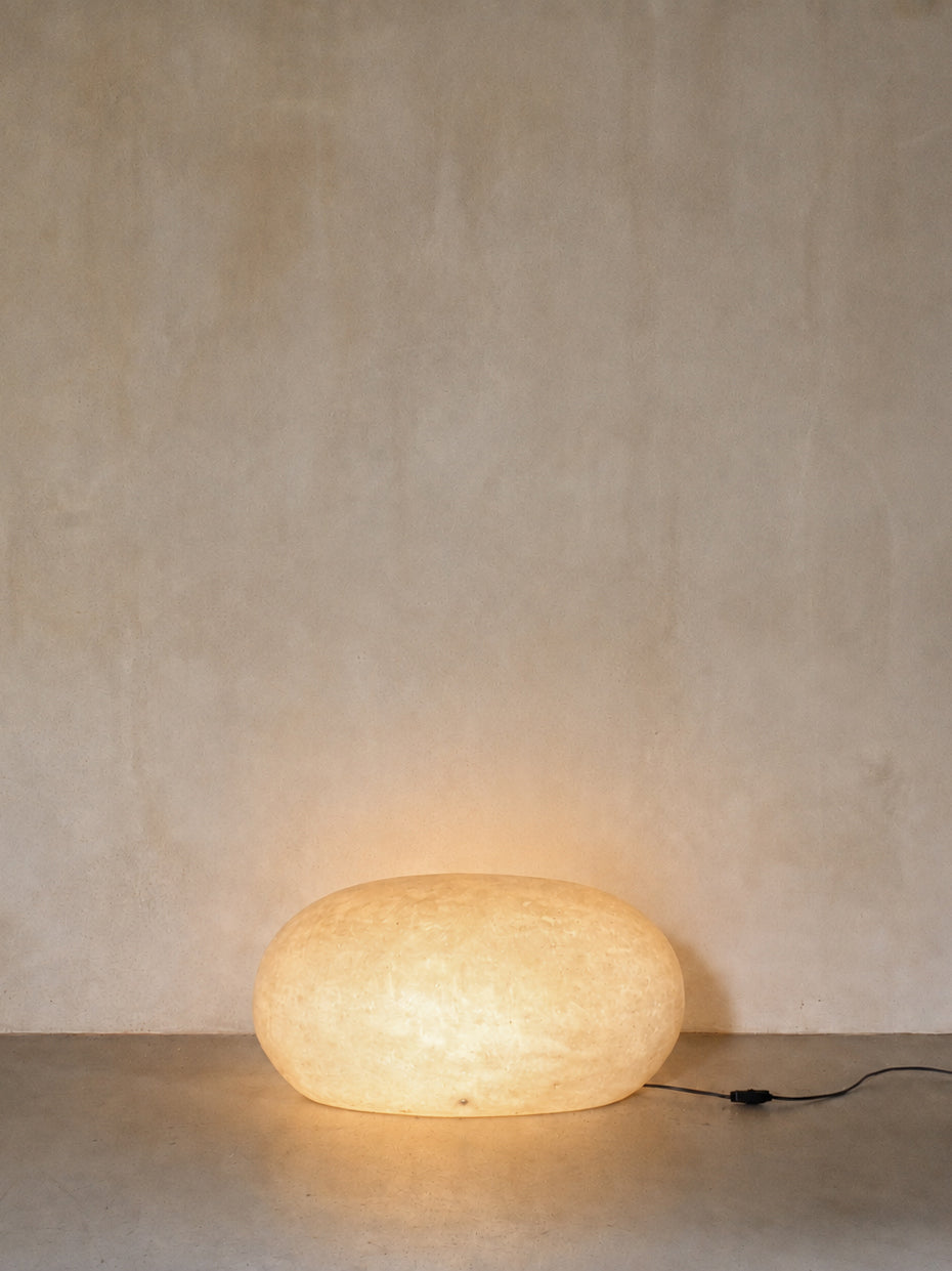 "Sasso" fiberglass lamp, lit, glowing against the plaster wall
