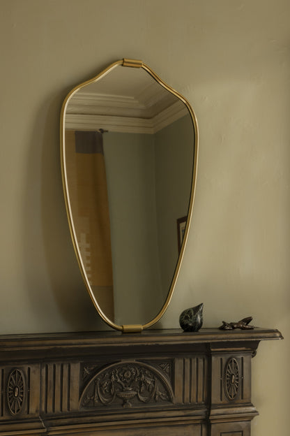 Senne Mirror in brass resting on a dark carved mantel in soft daylight