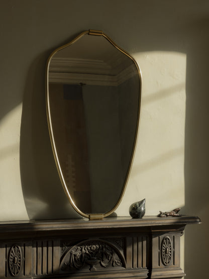 Senne Mirror in brass on a dark carved mantel with late sunlight and shadow across the wall