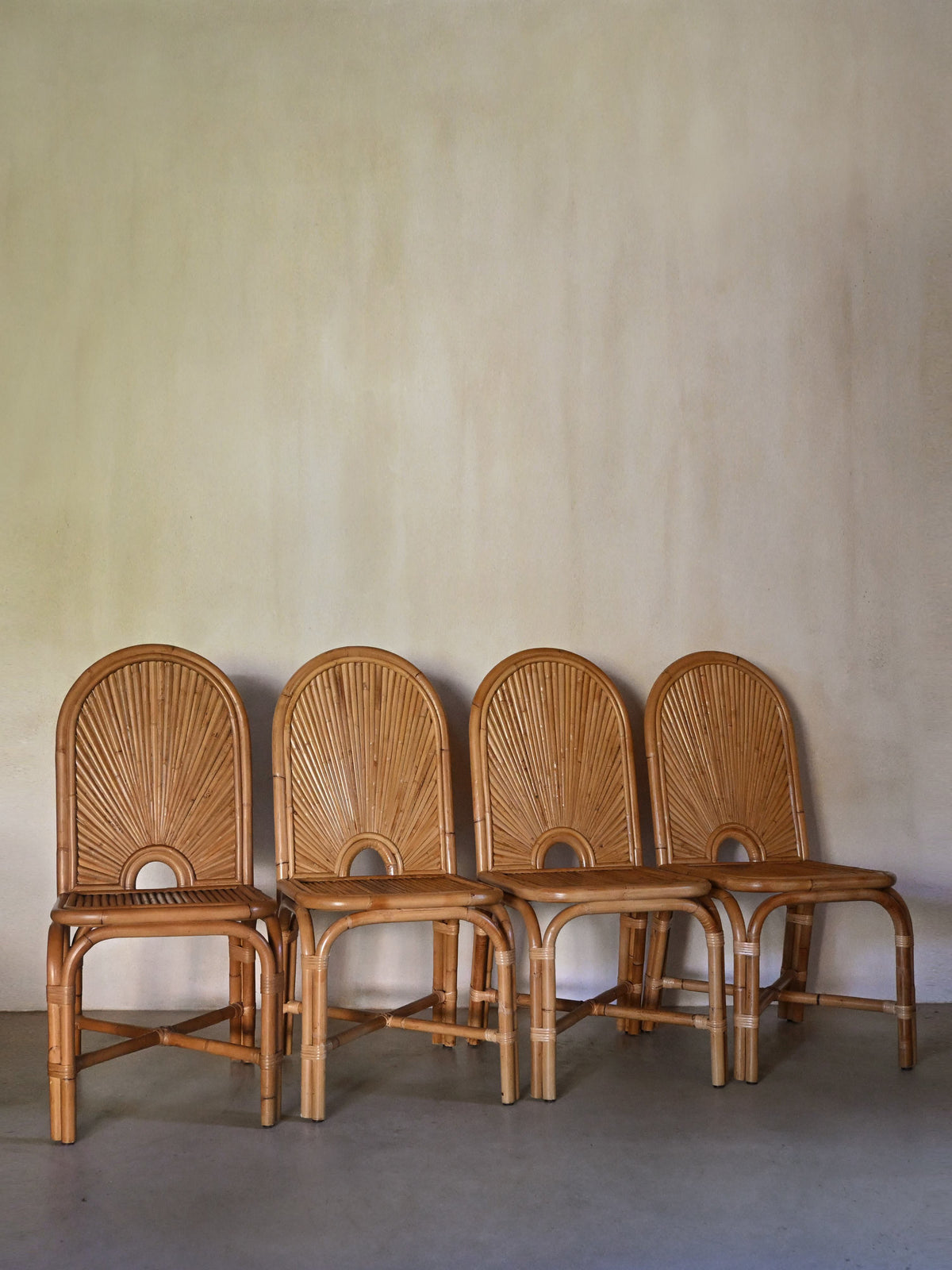 woven rattan chair, all four chairs lined against a plaster wall