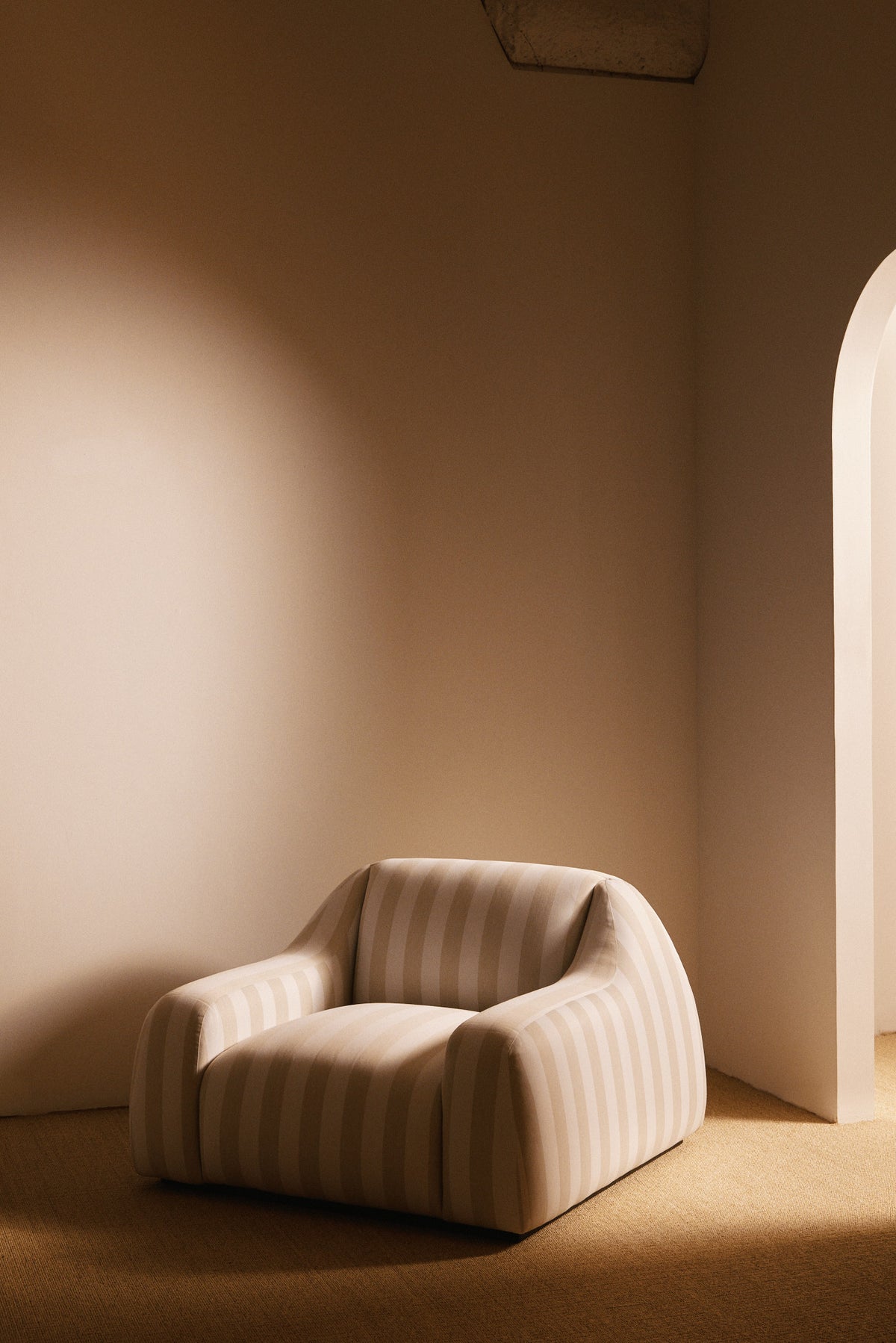 AS02 armchair in Jim Thomson Matelot Sea Shell fabric, distant angled view by an arched doorway