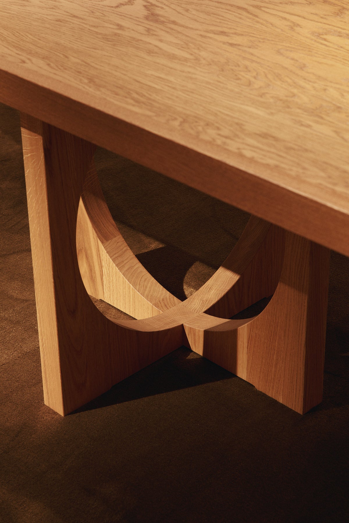 Moon dining table in solid oiled oak, close view of a leg with its circular opening and crossing bands