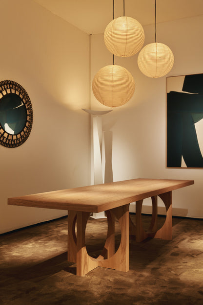 Moon dining table in solid oiled oak, view in a lit room under round pendant lights