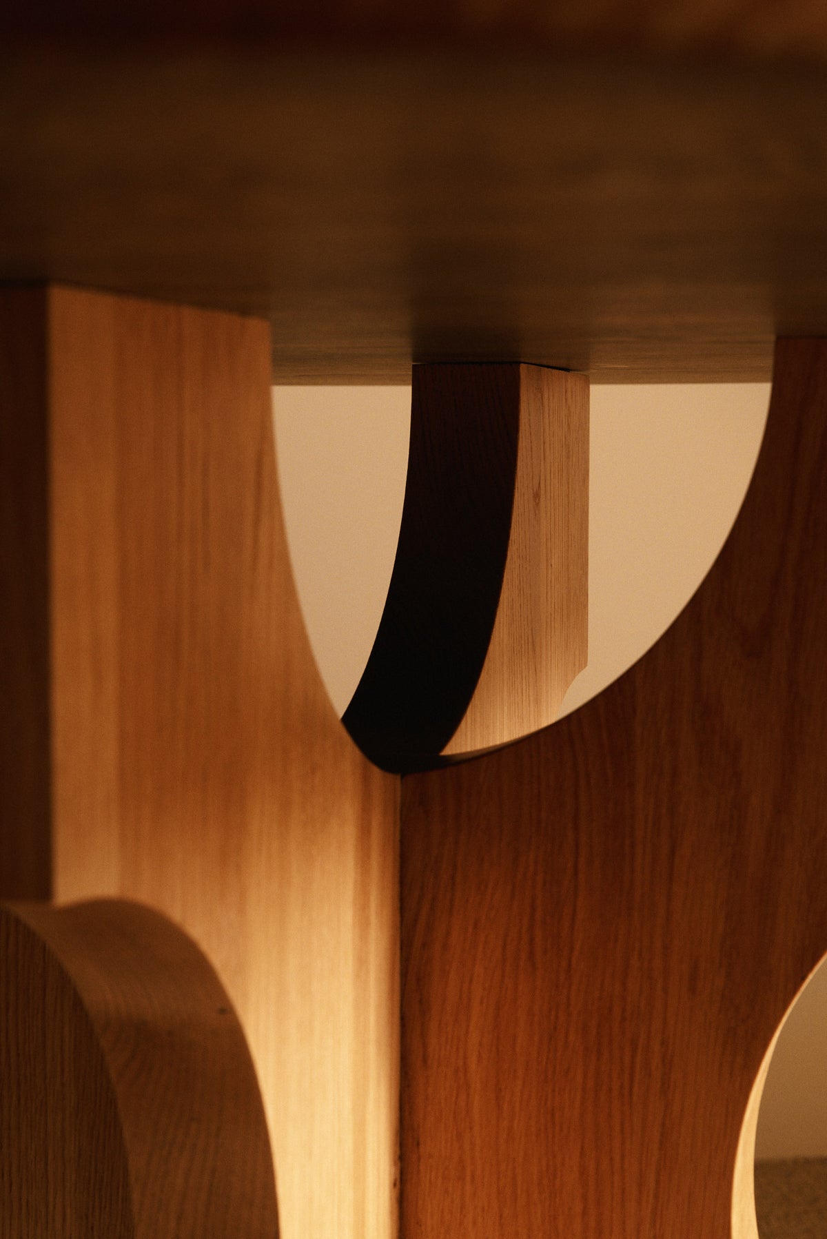 Orion round dining table in solid oiled oak, close view of an arch between the feet under the top