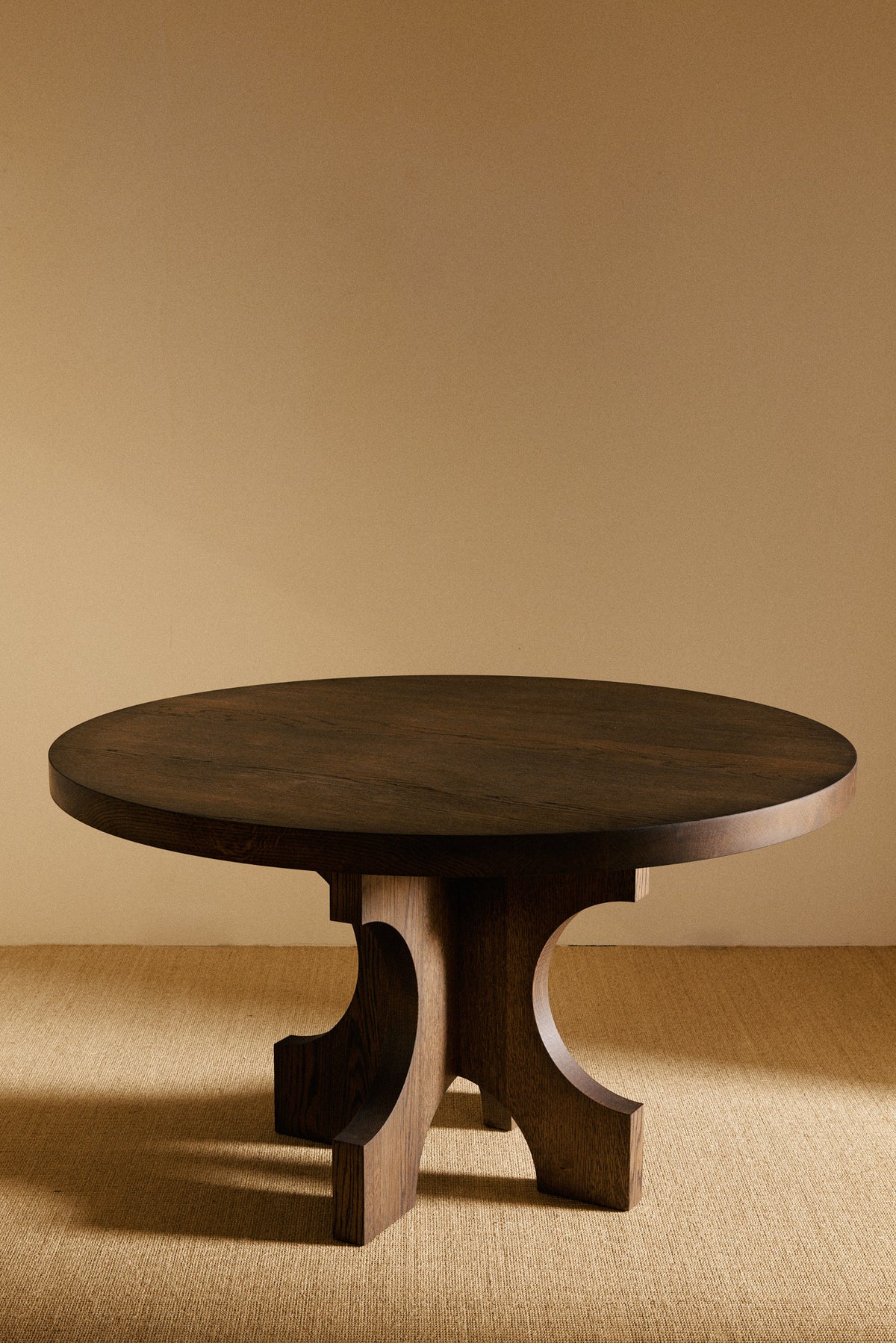 Orion round dining table in solid oiled oak, angled view of the table in a darker tone