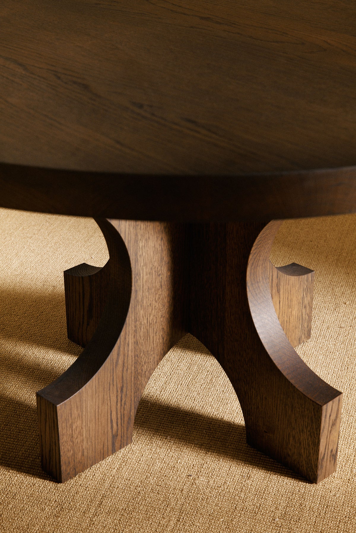 Orion round dining table in solid oiled oak, close view of the curved base in a darker tone