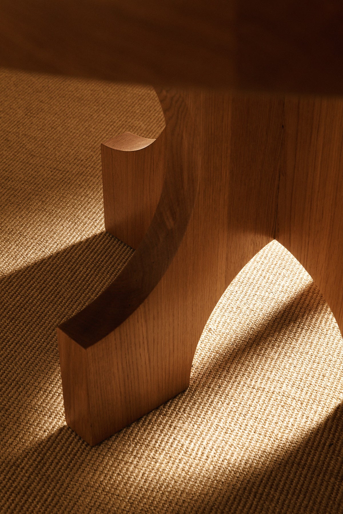 Orion round dining table in solid oiled oak, close view of a curved foot