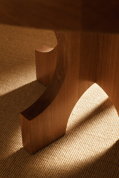 Orion round dining table in solid oiled oak, close view of a curved foot