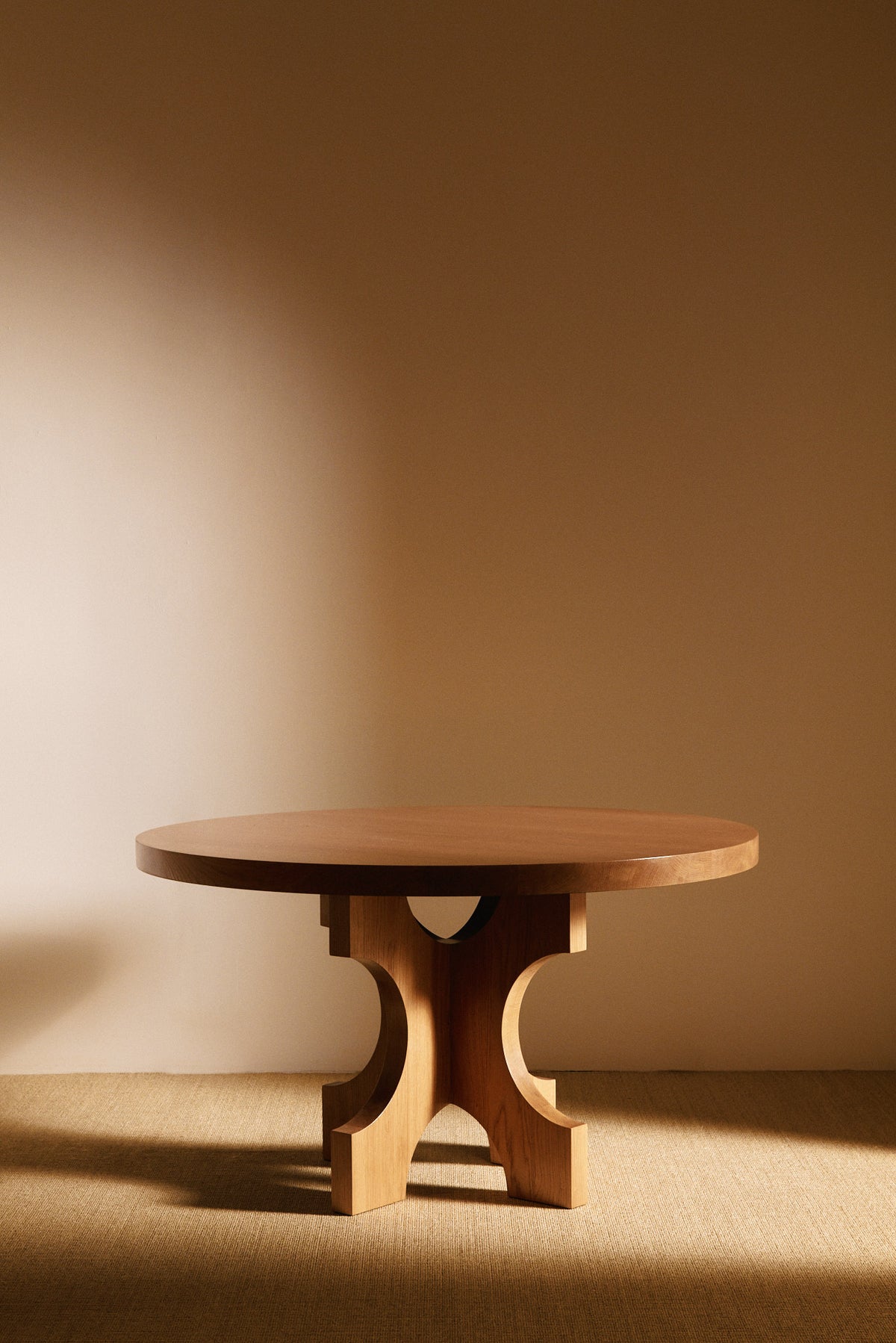Orion round dining table in solid oiled oak, front view with the arched base