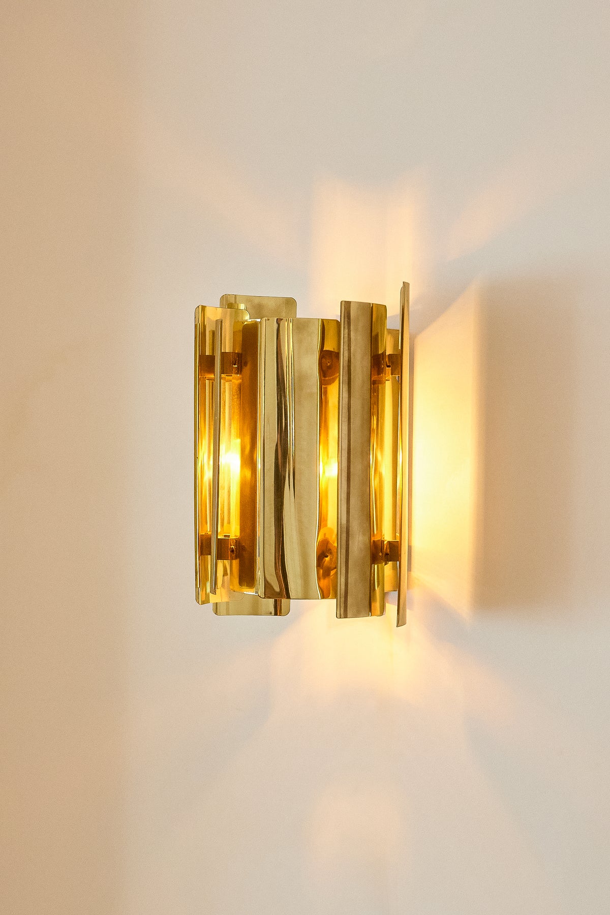 Falkenbergs Belysning brass sconce, lit on the wall with light spilling up and down