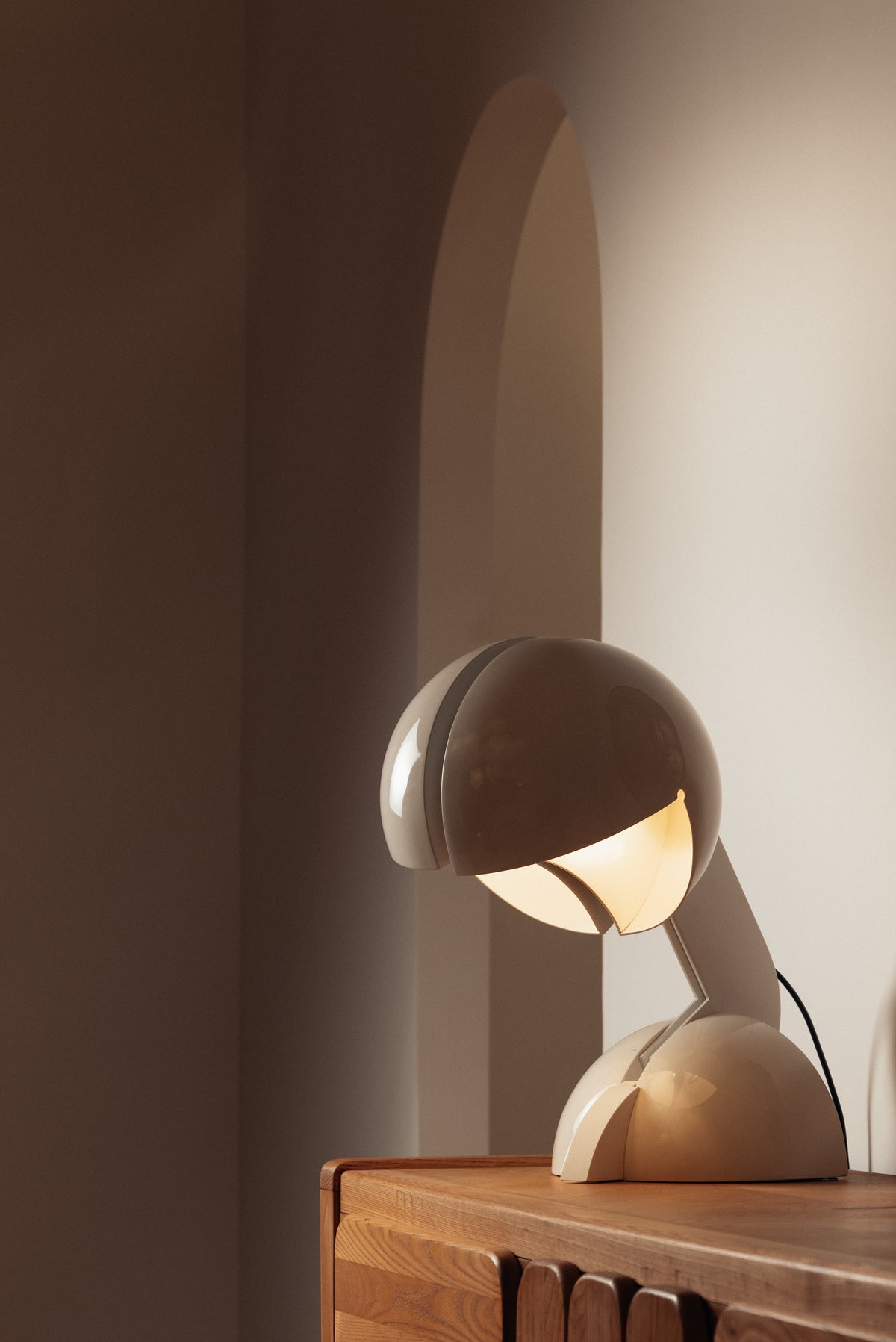 Gae Aulenti enameled aluminum Ruspa table lamp, lit on a cabinet in front of an arched niche