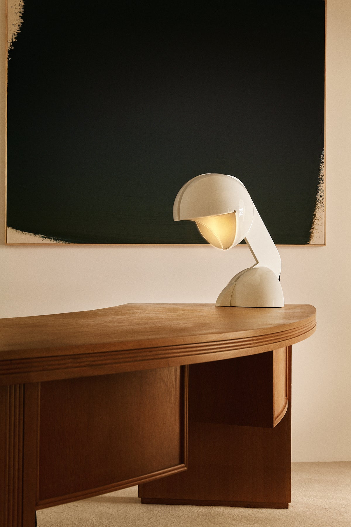 Gae Aulenti enameled aluminum Ruspa table lamp, on a curved desk in front of a dark painting