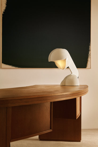 Gae Aulenti enameled aluminum Ruspa table lamp, on a curved desk in front of a dark painting