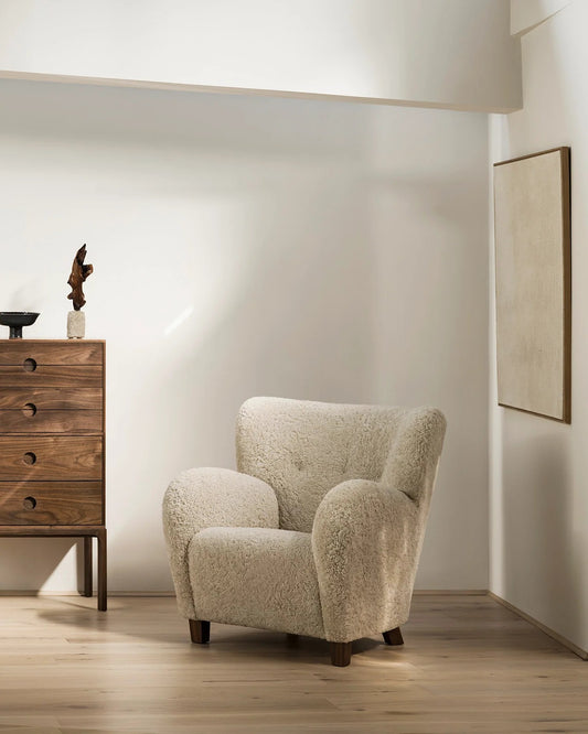 Karu Chair in Sheepskin Moonlight with walnut feet in a sunlit room beside a walnut chest