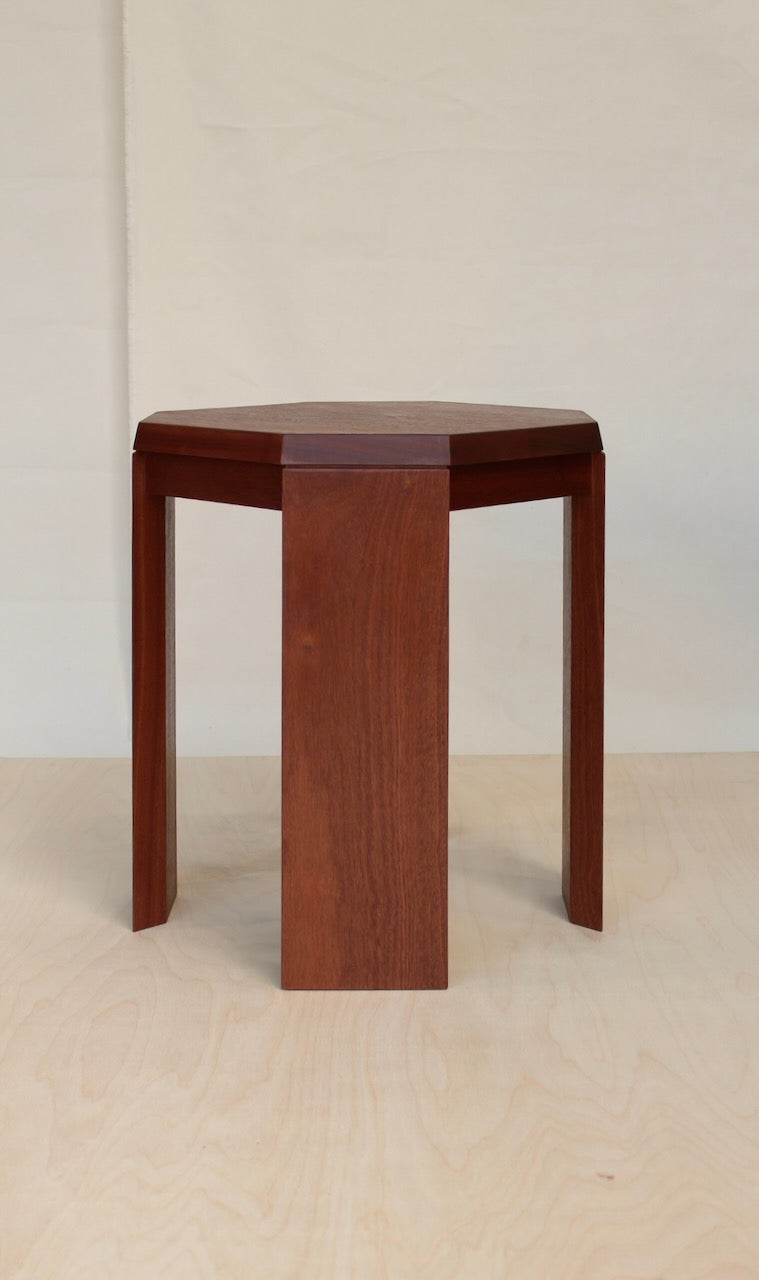 Paris Side Table in sapele mahogany, three quarter view of the octagonal top and flat slab legs on a pale birch floor